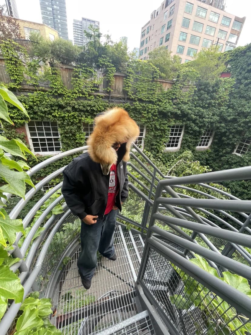 The Fox Pelt Jacket worn in profile, fox hood up, on a stairwell
